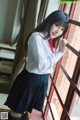 A woman in a school uniform leaning against a window.