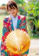 A woman in a colorful kimono holding a yellow fan.