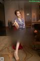 A woman in a red dress sitting at a table with a bowl of fruit.