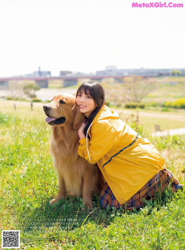 A woman in a yellow jacket sitting next to a dog in a field.
