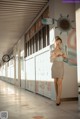 A woman in a white shirt and skirt standing in a hallway.