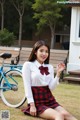 A woman in a school uniform sitting on the grass next to a bike.