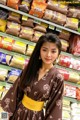 A woman in a brown kimono standing in front of a shelf of food.