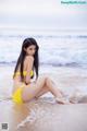 A woman in a yellow bikini sitting on the beach.