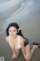 A woman in a white bikini sitting on the beach.