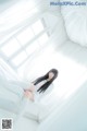 A woman sitting on a bed in a white room.