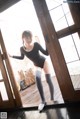 A woman in a black leotard and gray stockings posing in front of a window.