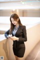 A woman in a black suit is looking at her phone.