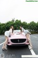 A couple of women standing next to a pink car.