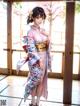 A woman in a pink kimono standing in front of a window.