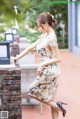 A woman in a dress leaning against a brick wall.